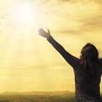 Person holding hands in air while looking at sun